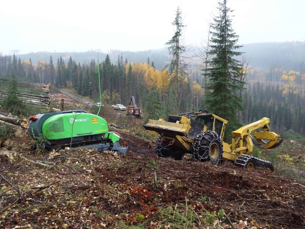 T-WINCH 10.2 tethered to a yellow wheel loader in a job site in a forest